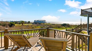 A wooden deck with chairs overlooking a beach and a building in the distance. - Steps from the Beach!  (Crystal Beach)