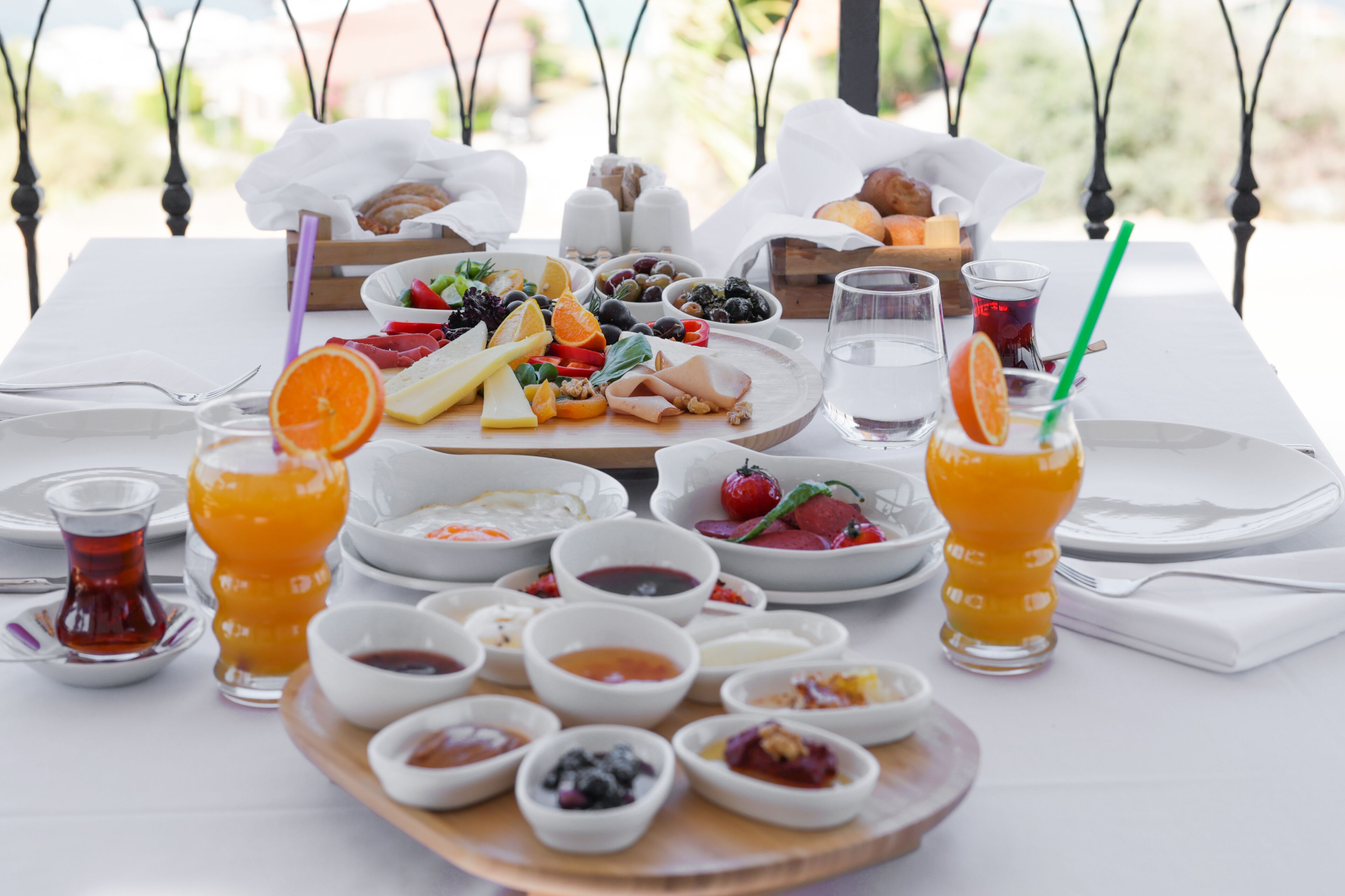 A table set with a variety of food items and drinks, including fruits, cheeses, and condiments, arranged on a white tablecloth.