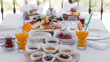 A table set with a variety of food items and drinks, including fruits, cheeses, and condiments, arranged on a white tablecloth.