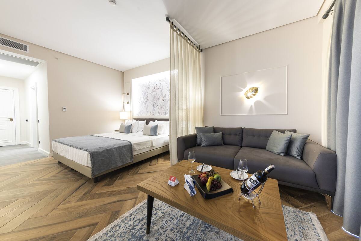 A modern hotel room with a bed, sofa, wooden coffee table, and a wall-mounted light fixture.