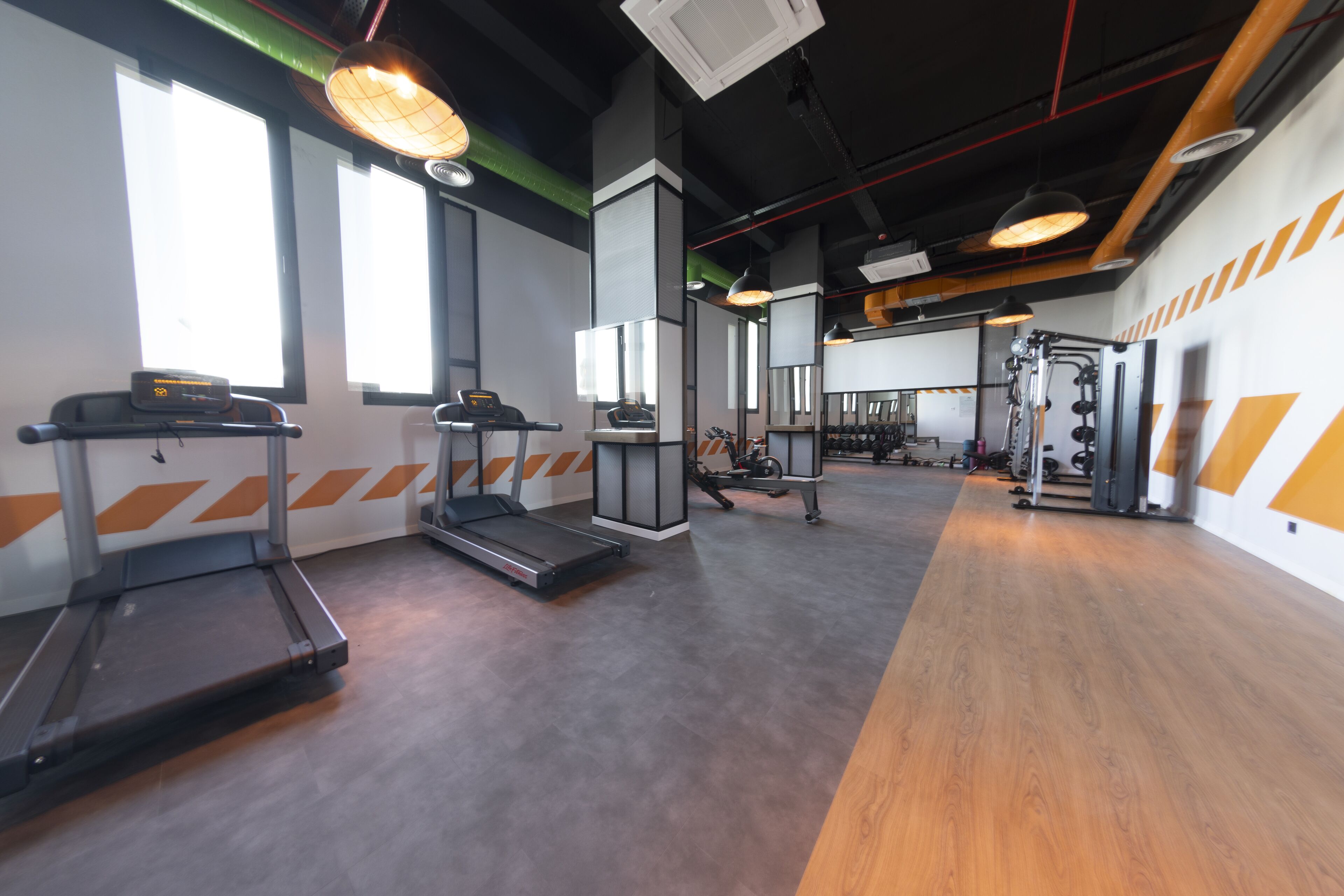 Un gimnasio con cintas de correr, zona de pesas y ventanas amplias.