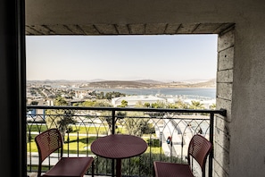 A balcony with two chairs and a table, overlooking a cityscape with buildings and a body of water. - Soliport Hotel & Spa (Cesme)