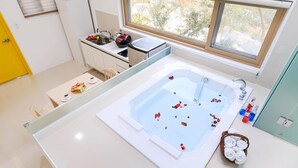 A modern bathroom with a large bathtub, a window, and a small kitchen area. - Ganghwa Nolang Pension (Incheon)