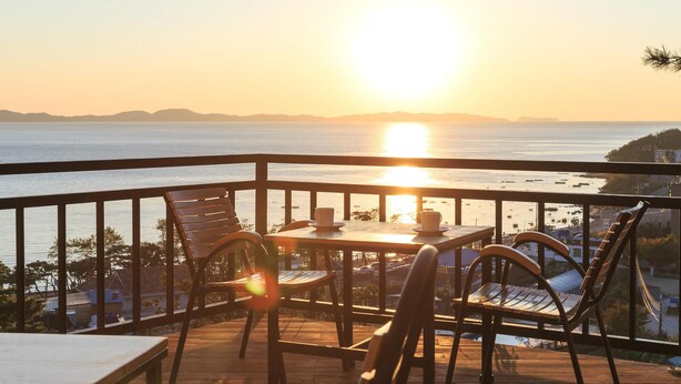 A balcony with a table and chairs overlooking a body of water during sunset. - Ganghwa Nolang Pension (Incheon)