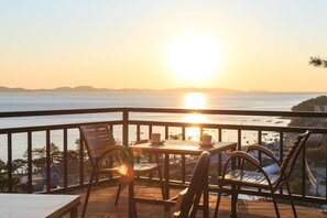 A balcony with a table and chairs overlooking a body of water during sunset.