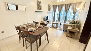 A dining area with a table set for four, a television, and a sofa with a plant. - LKV - 1bed with 2 balconies in JLT (Dubai)