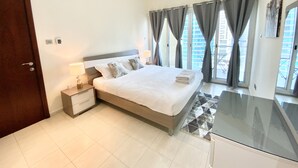 A modern bedroom with a large bed, bedside tables, a desk, and a view of a cityscape through large windows. - LKV - 1bed with 2 balconies in JLT (Dubai)