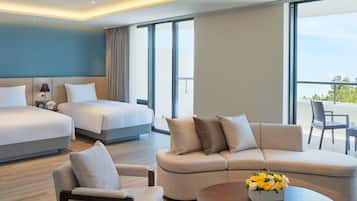 A modern hotel room with two beds, a sofa, a coffee table, and a balcony with outdoor seating.