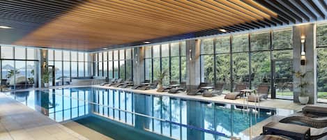Una piscina interior moderna con sillones de descanso y grandes ventanales que ofrecen vistas al exterior.