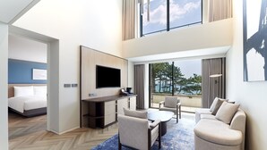 A modern hotel room with a large bed, a TV, a desk, and a seating area with a view of the outdoors. - Parnas Hotel Jeju (Seogwipo)