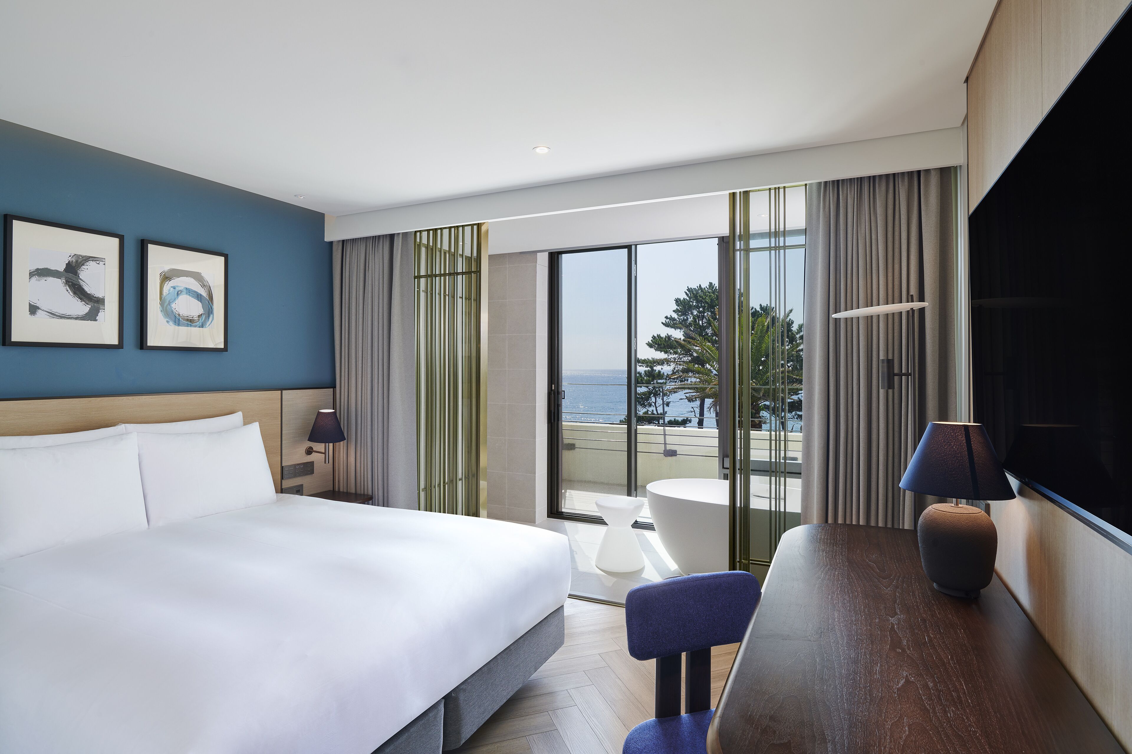 Camera d'albergo con un letto grande, una scrivania con lampada, una TV e vista sull'oceano.