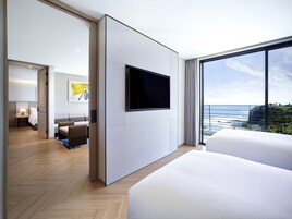 Una habitación de hotel moderna con una cama grande, un televisor de pantalla plana montado en la pared y un balcón con vista al océano.