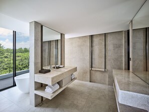 A modern bathroom with a large bathtub, a vanity with a mirror, and a view of greenery outside.