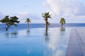 A pool with clear blue water, surrounded by palm trees and a view of the ocean. - Parnas Hotel Jeju (Seogwipo)