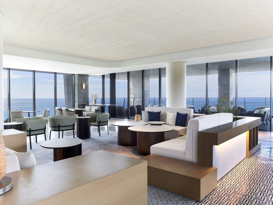 A modern lounge area with seating, tables, and large windows overlooking the ocean.
