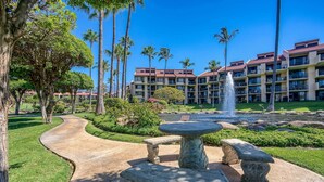 A courtyard with a fountain, palm trees, and a building with balconies. - Maui Paradise: Steps to Sand-Blg#1. Partial Ocean View, AC's, Wifi, 1st Floor (Kihei)