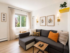 A modern living room with a grey sectional sofa, a small wooden coffee table, and a window with curtains.