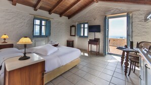 A bedroom with a bed, bedside lamps, a television, and a view of the outside. - Lithos Stone Suites (East Mani)