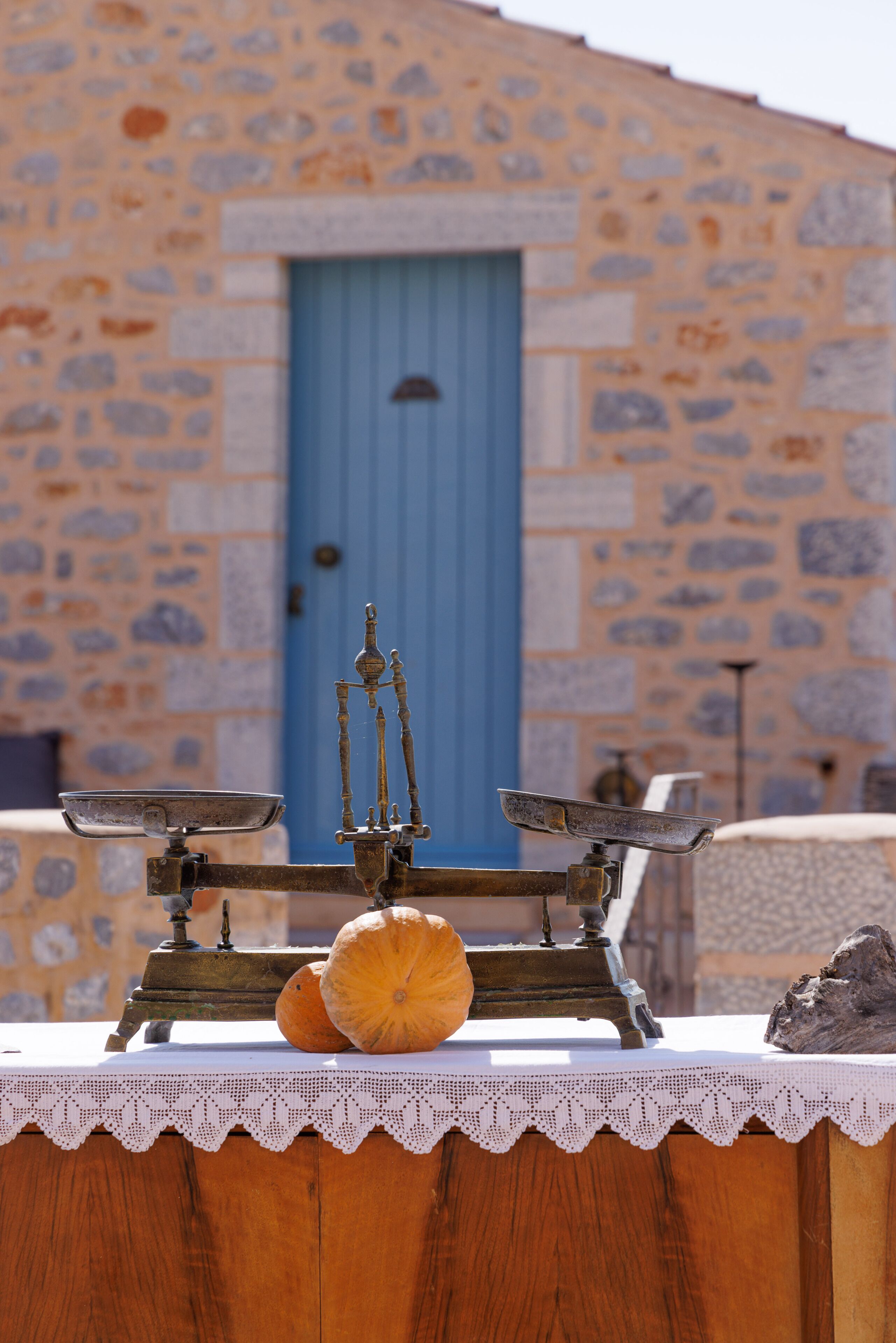 A rustic stone building with a blue door, a wooden table with a white lace tablecloth, and two pumpkins on the table.