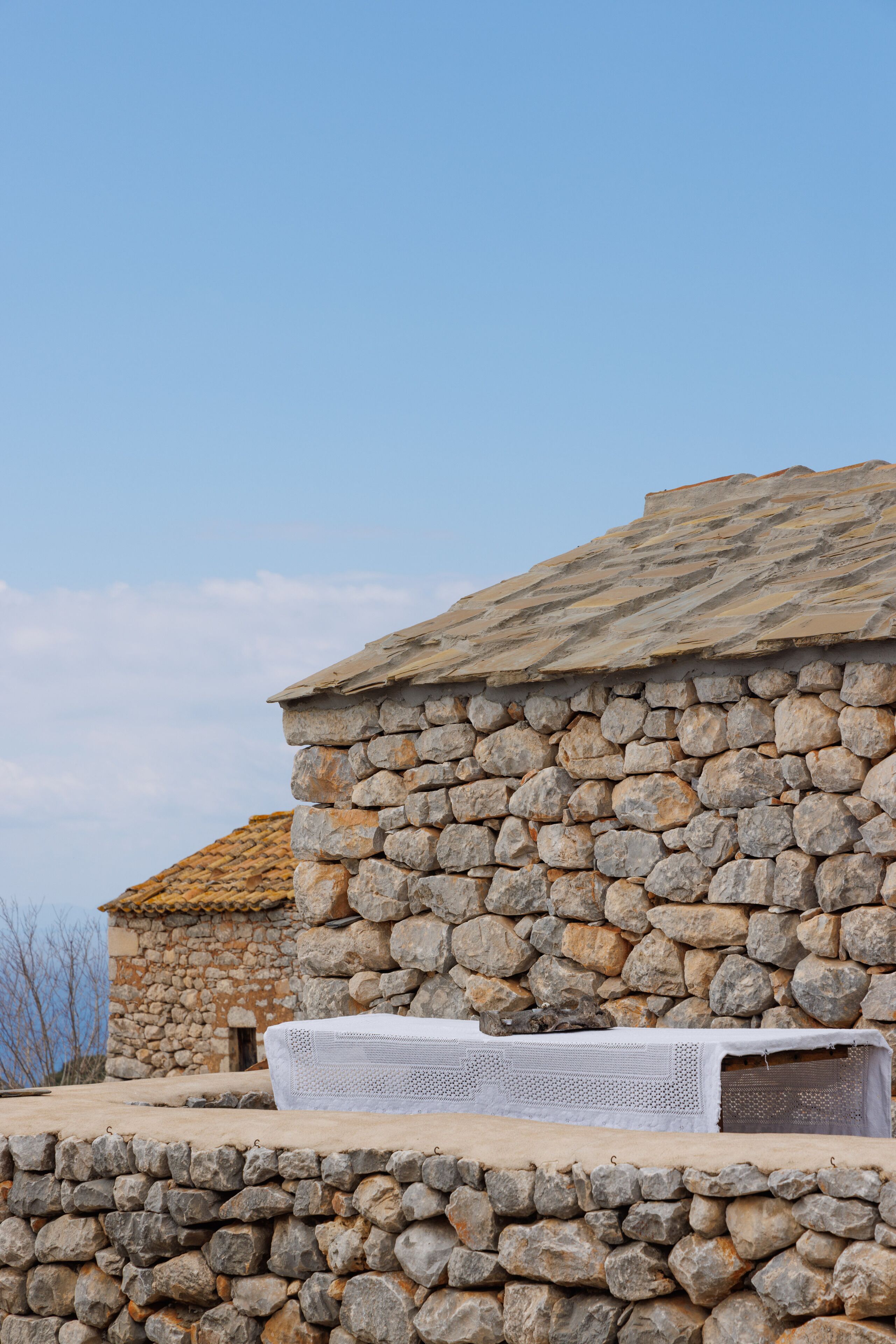 A stone building with a tiled roof and a white bench in front.