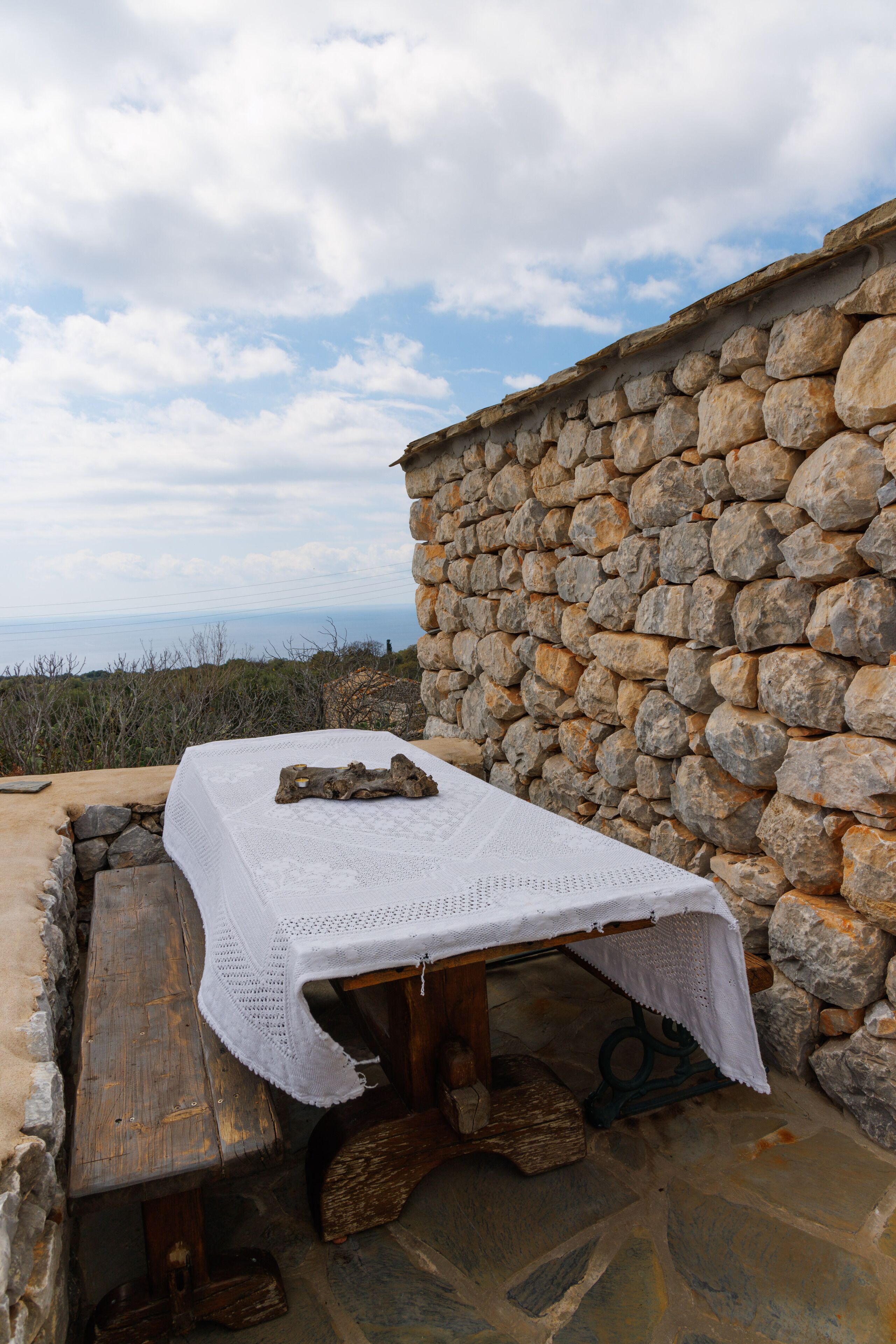 A stone wall with a wooden bench and a table covered with a white cloth.