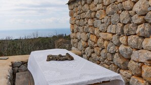 A stone wall with a wooden bench and a table covered with a white cloth. - Lithos Stone Suites (East Mani)