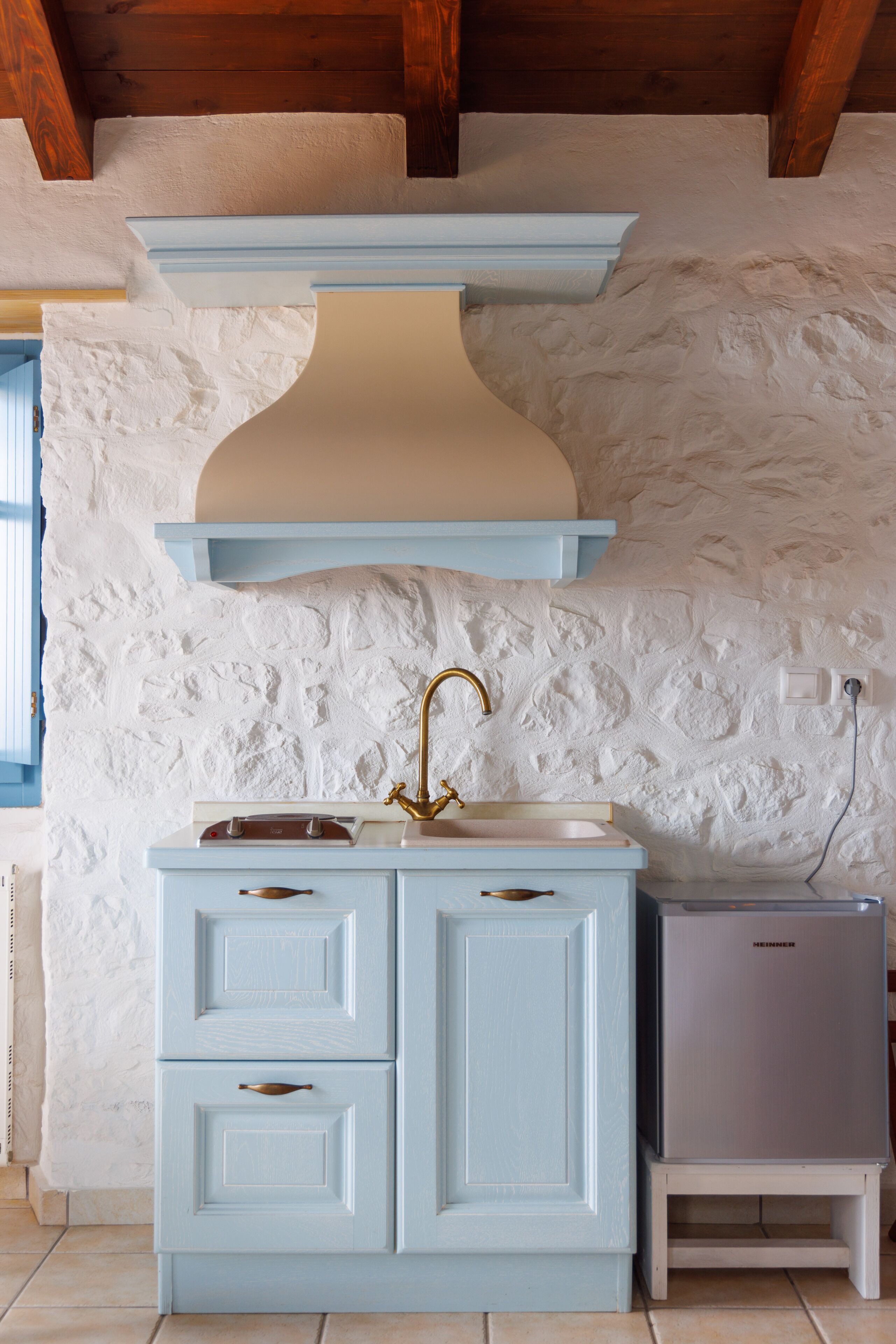 A kitchen with a white textured wall, a blue cabinet, a gold faucet, and a small refrigerator.