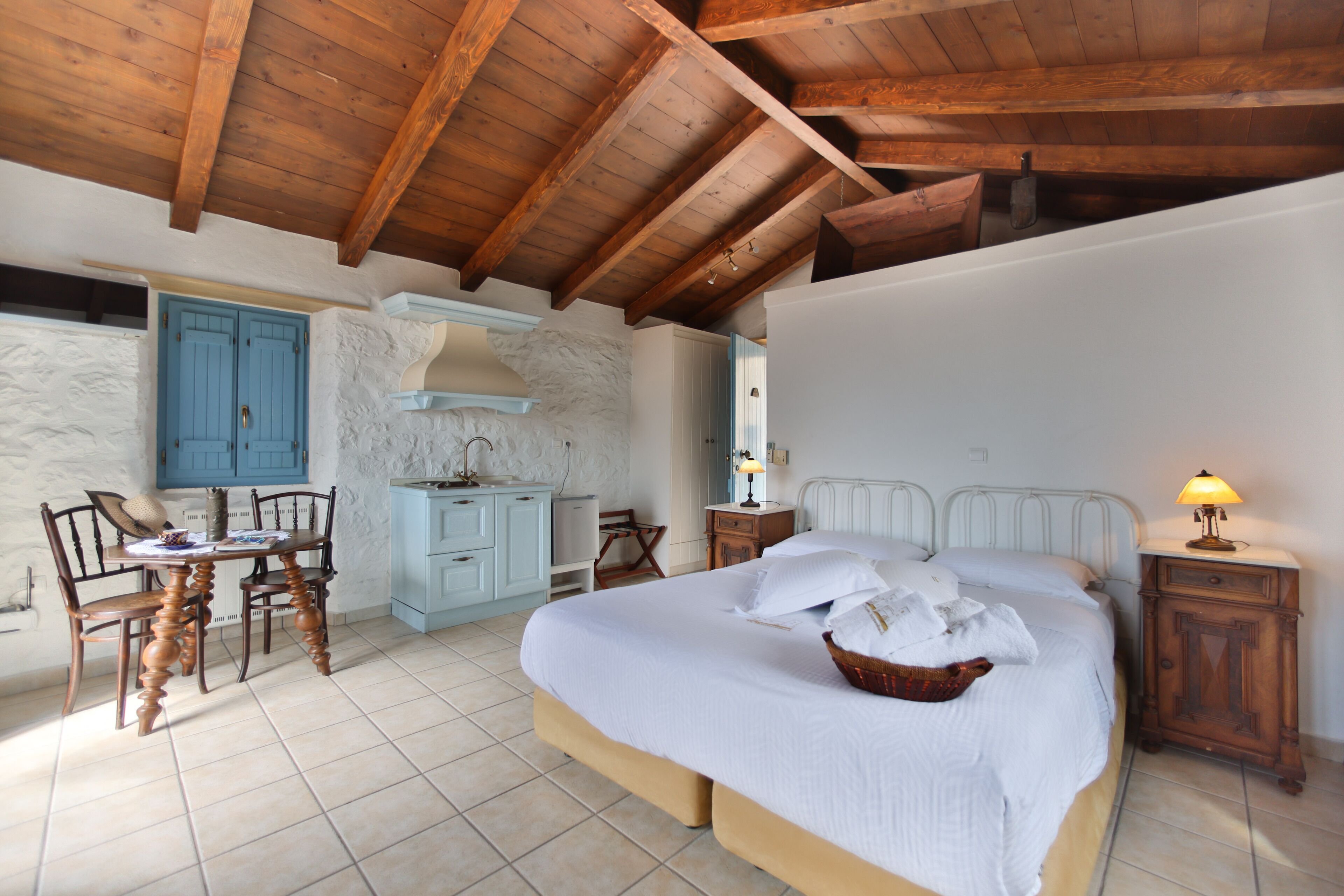 Un dormitorio con una cama grande, techo de madera, un pequeño rincón de cocina y una mesa de comedor con sillas.