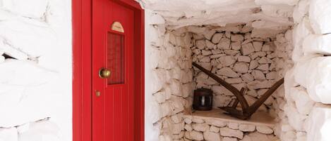 A red door with a stone wall and a wooden shelf.