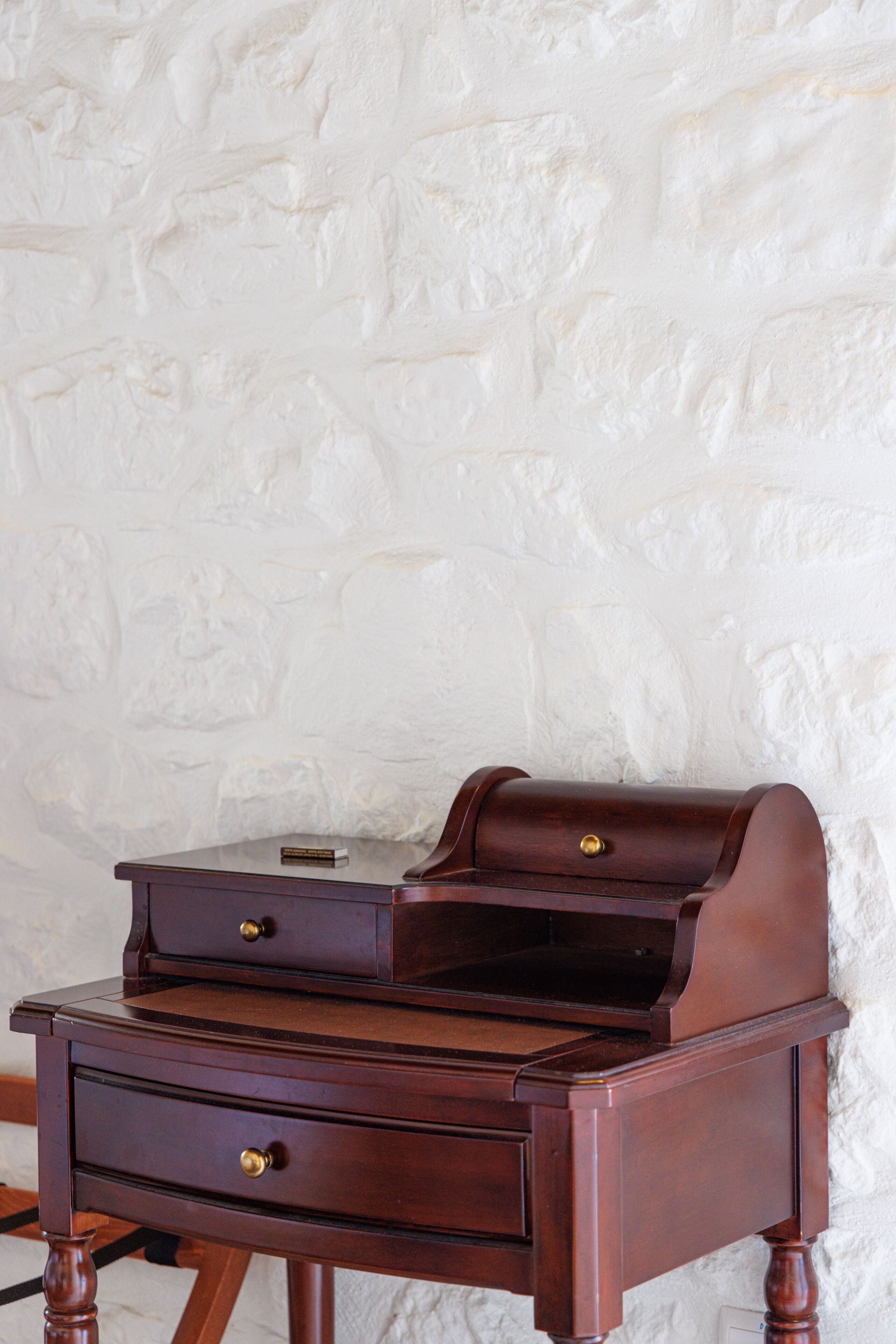 A wooden desk with drawers and a printer, against a textured white wall.