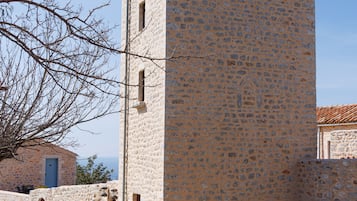 Una torre de piedra con una entrada estrecha y una puerta pequeña, rodeada por una calle empedrada y un árbol.