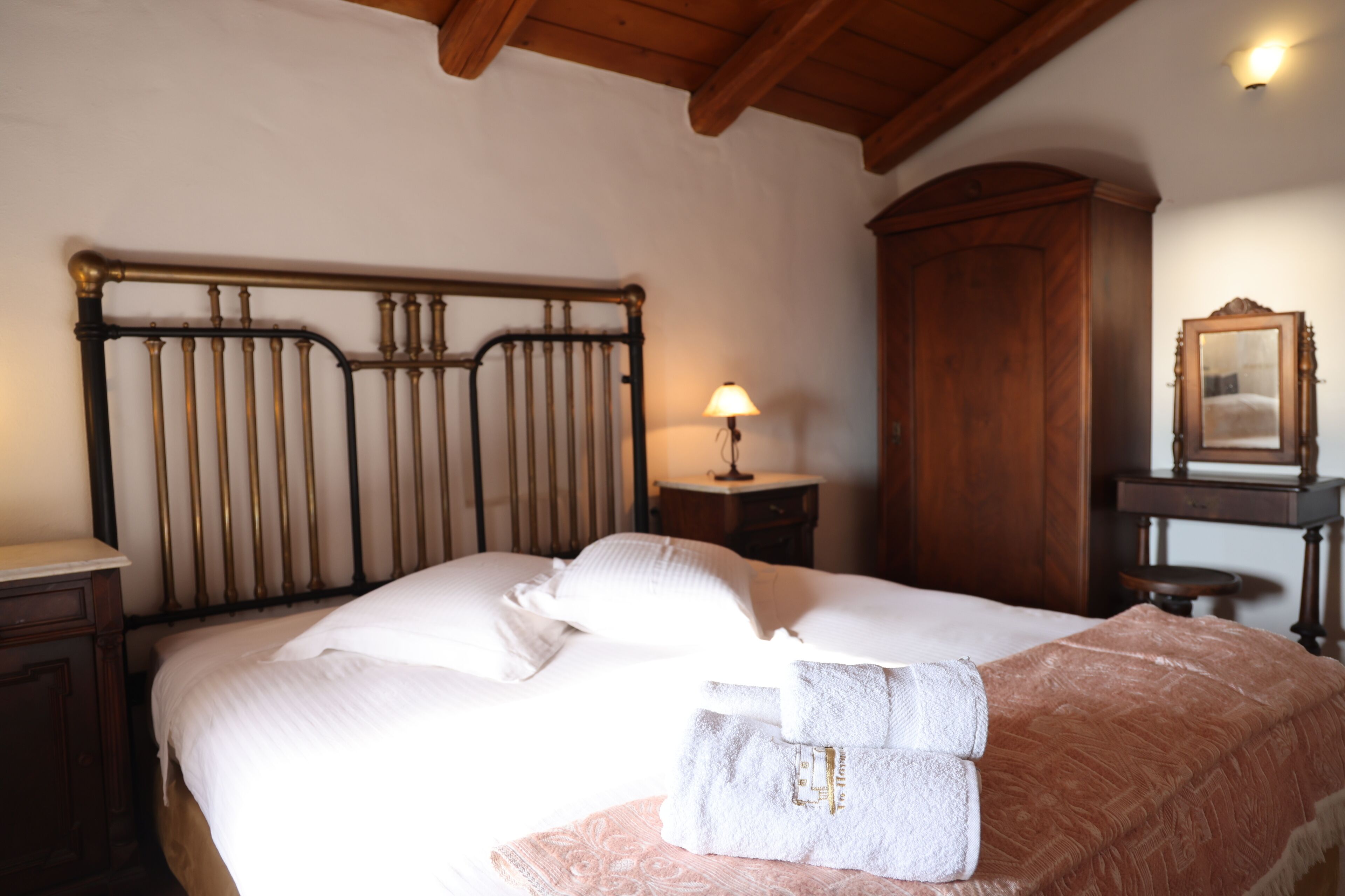 A bedroom with a bed, a nightstand, a lamp, a wooden wardrobe, and a mirror.