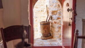 Un arco de entrada que da a una habitación de paredes de piedra, con un balde de madera rústico y herramientas.