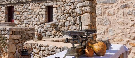 A rustic stone building with a wooden table covered by a white cloth, featuring a lantern, a knife, and pumpkins.