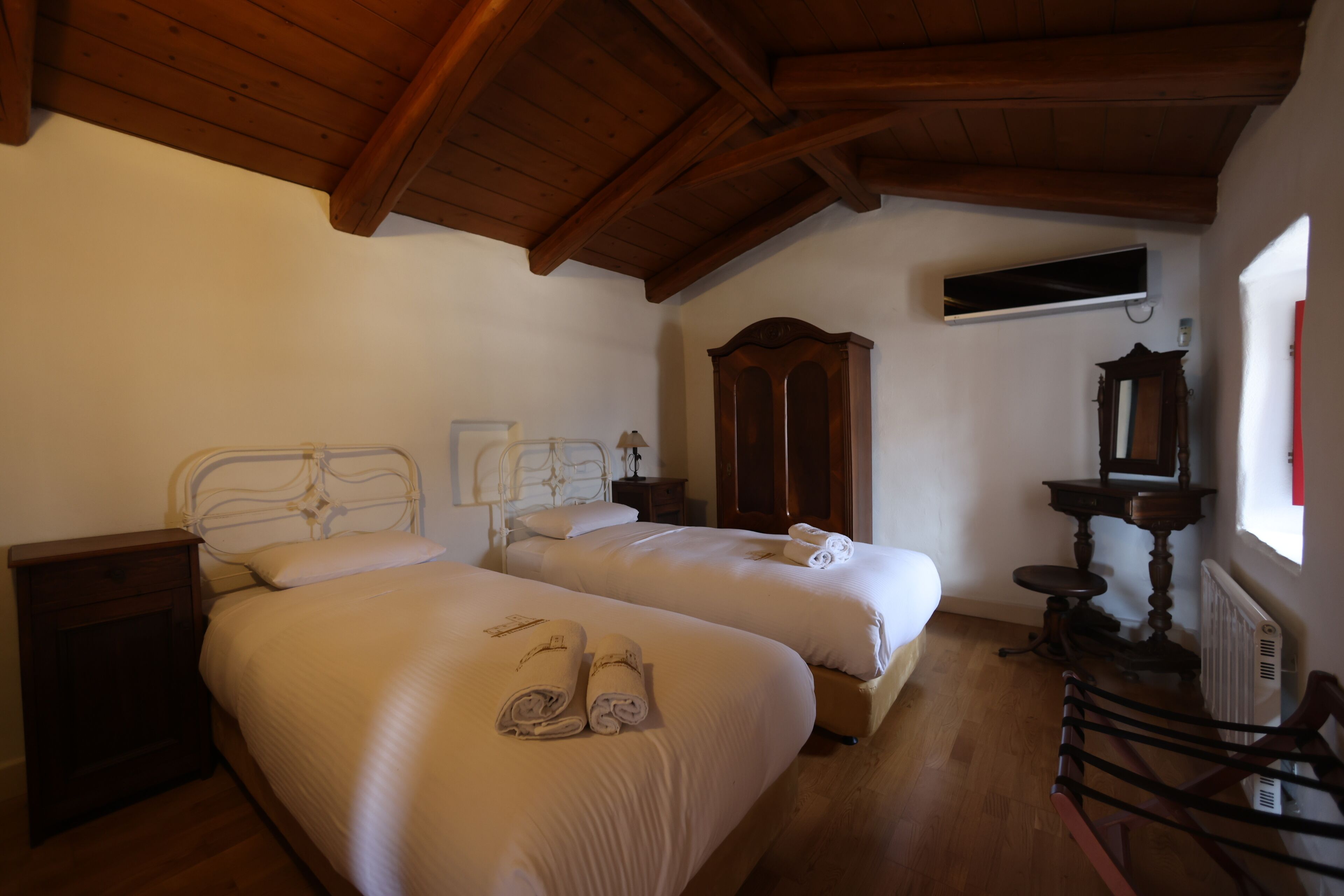 Un dormitorio con dos camas, cabeceros de madera, un aparador de madera, un espejo y un radiador.