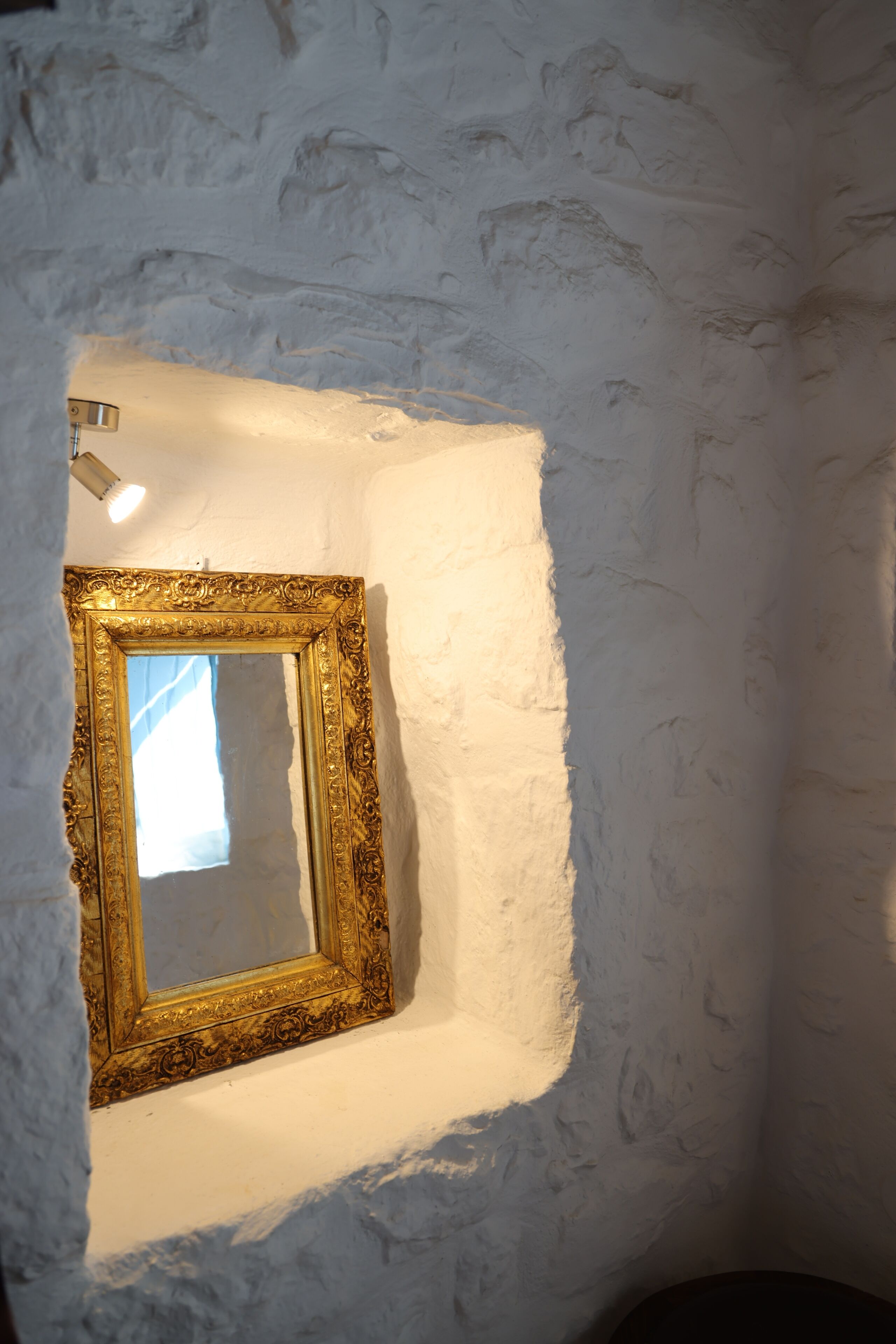 A corner of a room with a textured white wall and a gold-framed mirror.