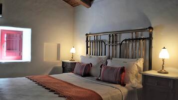 A bedroom with a bed, two bedside tables with lamps, a window with a view, and a wooden ceiling.