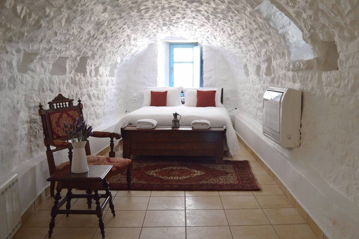 A cozy room with a bed, a wooden chair, a small table, and a radiator.