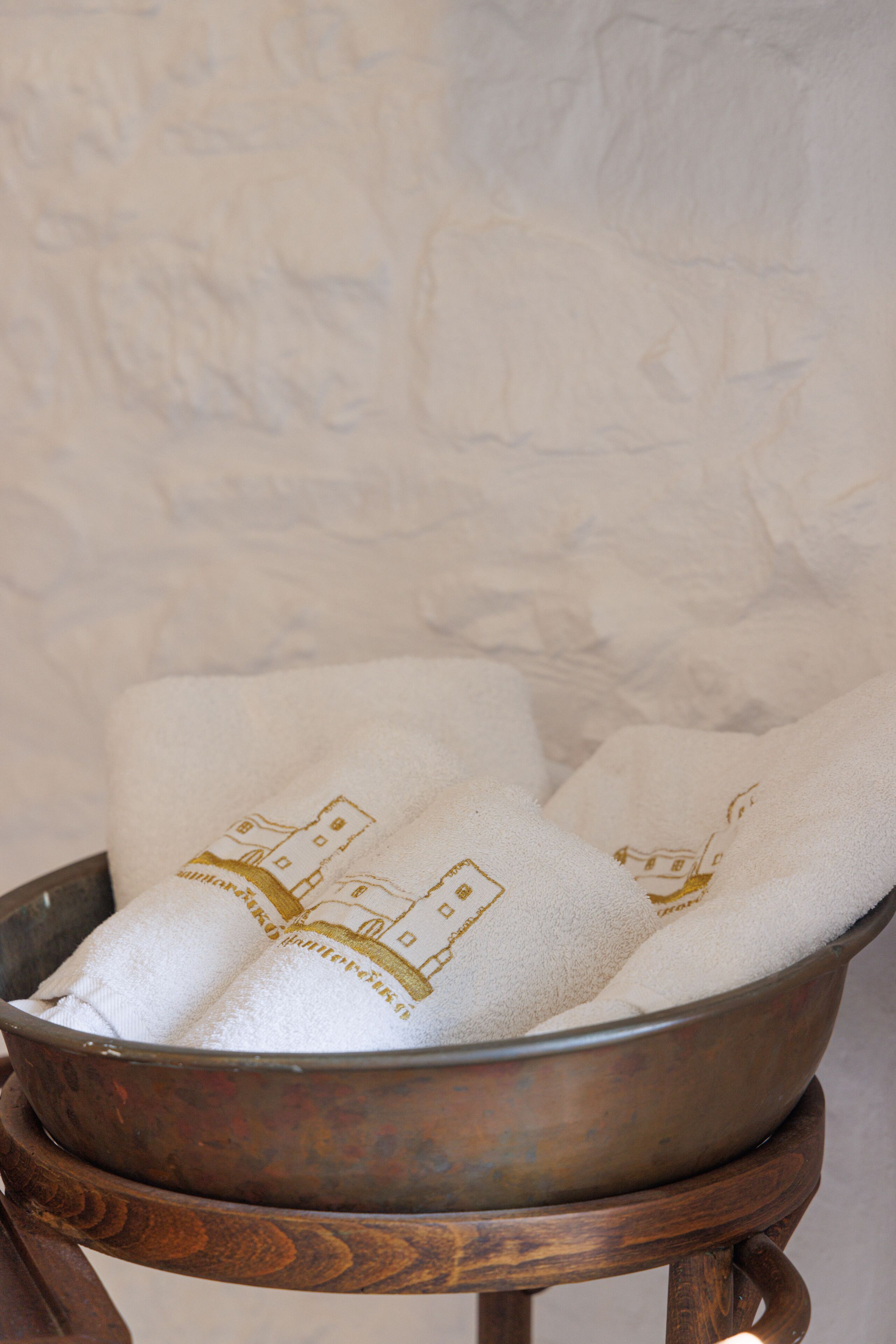 A metal bowl with a white towel featuring a building design, placed on a wooden stand.