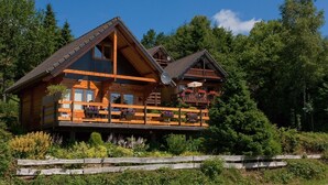 A wooden cabin with a balcony, surrounded by lush greenery. - Escape in Dochamps Chalet (Manhay)