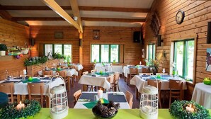 A cozy, wooden-floored dining area with tables set for a meal, surrounded by windows and greenery. - Escape in Dochamps Chalet (Manhay)