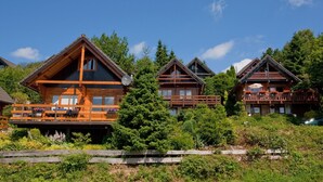 A row of wooden cabins with balconies, surrounded by lush greenery and trees. - Escape in Dochamps Chalet (Manhay)