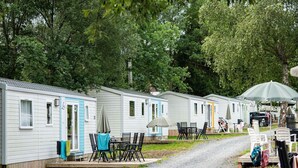 Een rij mobiele woningen met buitenruimtes, elk voorzien van een tafel en stoelen.