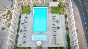 An aerial view of a rectangular swimming pool with lounge chairs and umbrellas, surrounded by greenery and a paved walkway. - AST - Modern studio flat with balcony (Dubai)