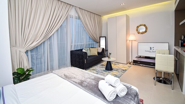 A modern hotel room with a large bed, a sofa, a small table, a TV, and a desk area. - AST - Modern studio flat with balcony (Dubai)