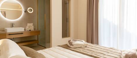 A modern hotel room with a bed, a bathroom with a sink and mirror, and a glass shower door.