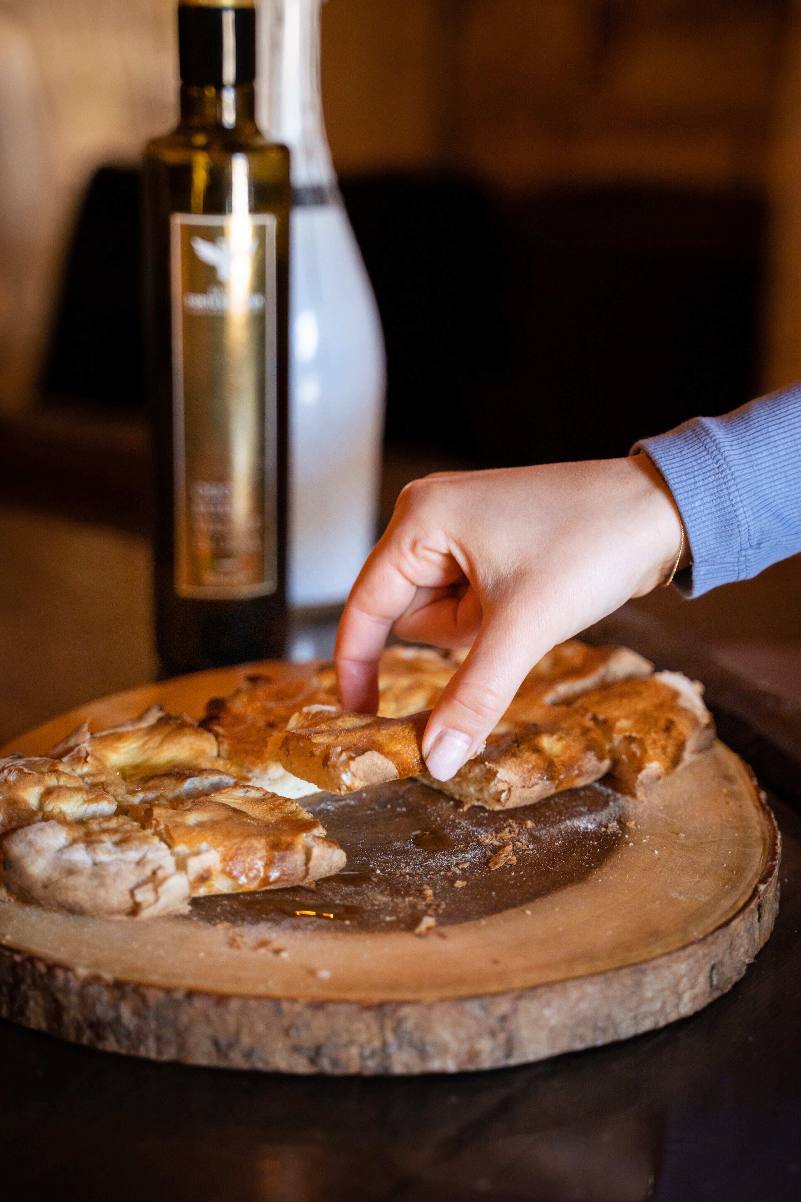 A hand placing a piece of pizza on a wooden board.