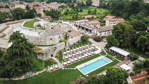 Vista aérea de uma villa histórica com piscina, jardins exuberantes e paisagem montanhosa ao fundo.