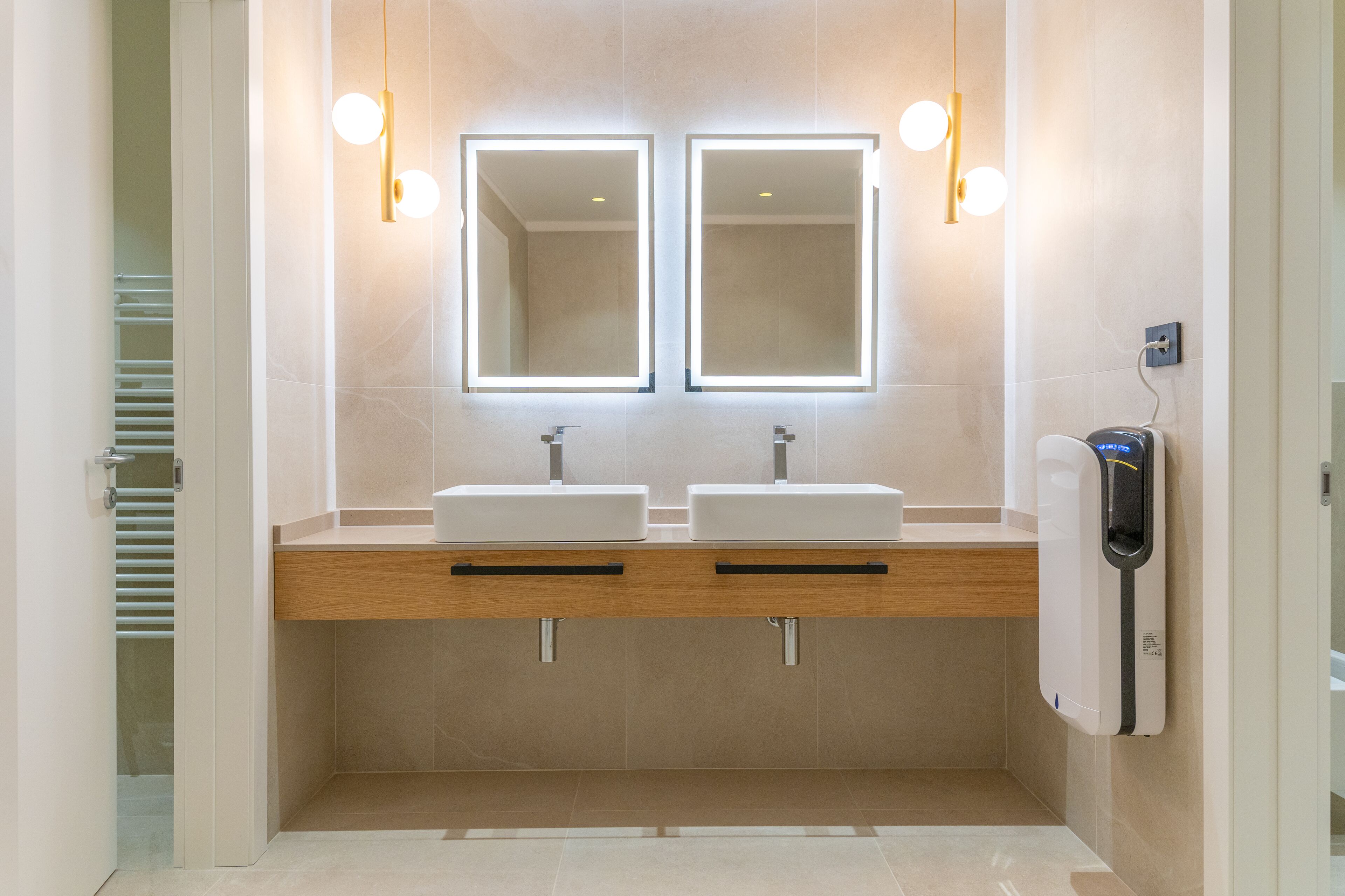 Un bagno moderno con due lavabi, uno specchio e un asciugamani ad aria.
