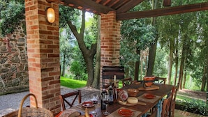 Un espacio de comedor al aire libre con pared de ladrillo, mesa y sillas de madera.